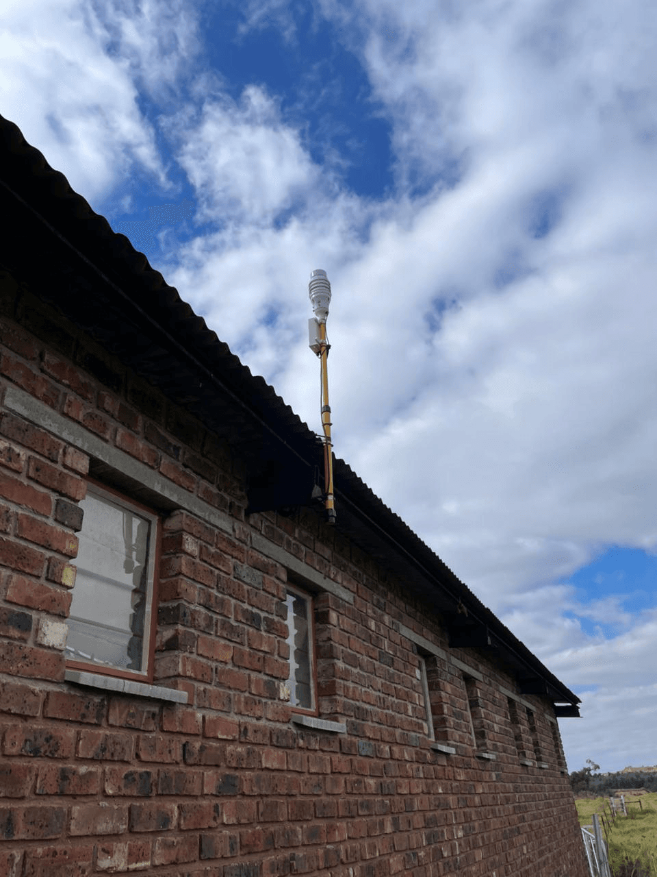 KyberMini environmental monitoring unit mounted on a building wall under an open sky.