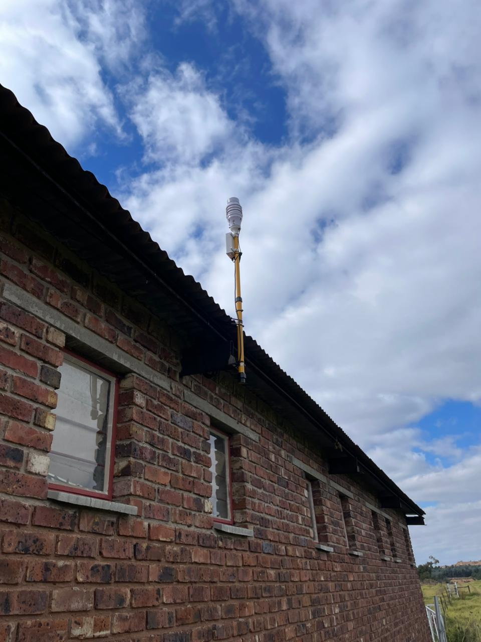 KyberMini environmental monitoring unit mounted on a building wall under an open sky.